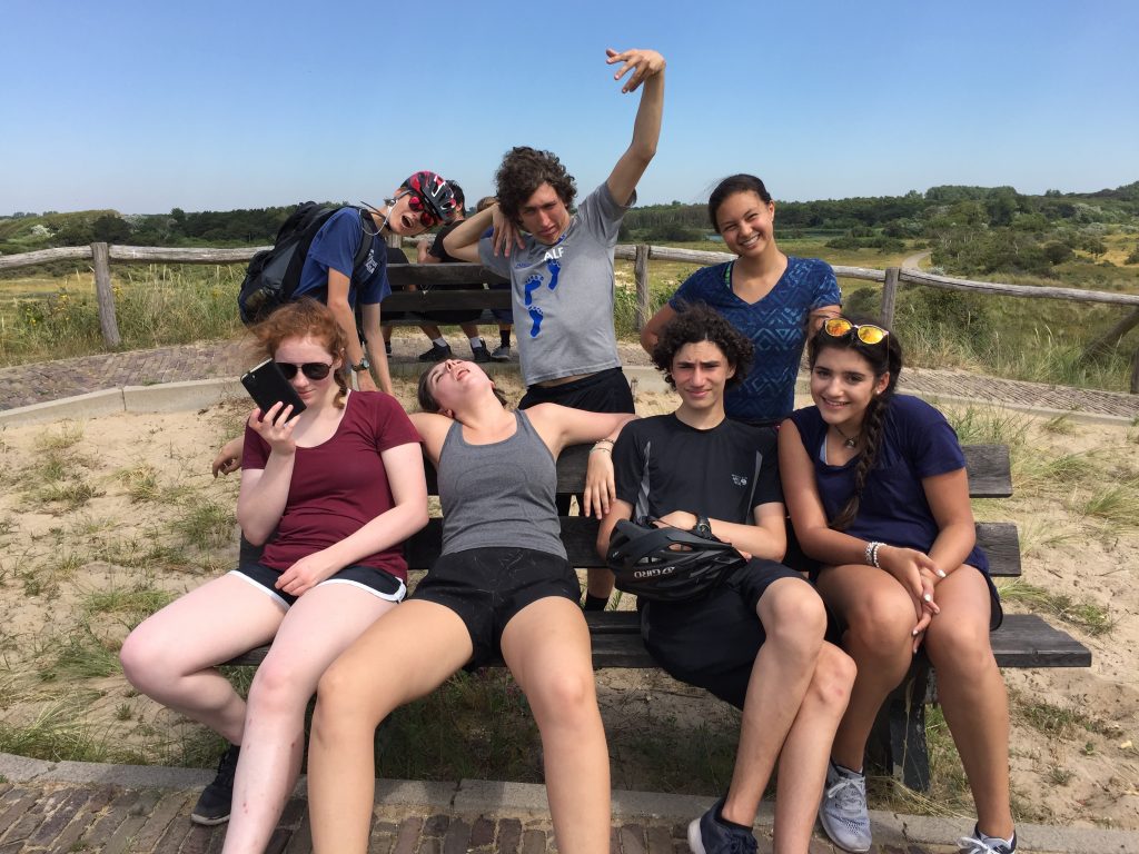 Sam, Kaes, Kelsey, Maggie, Taylor, Jacob, and Nikki channel their expressions of the moment on or around a park bench by the Dutch seaside.